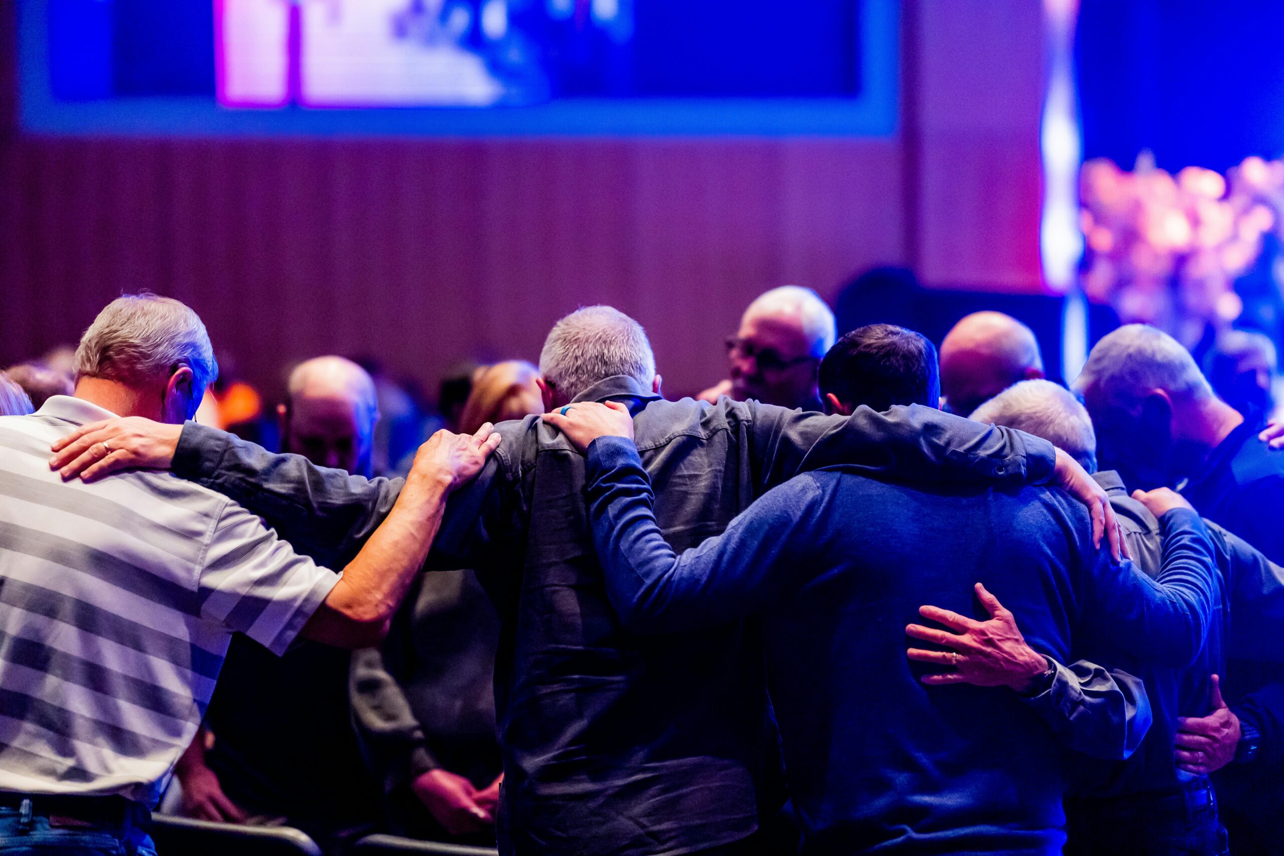 A congregation of men embracing and praying together in a church setting.